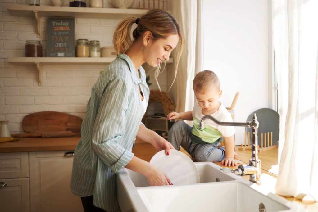 Mother washing dishes at the kitchen sink with her baby